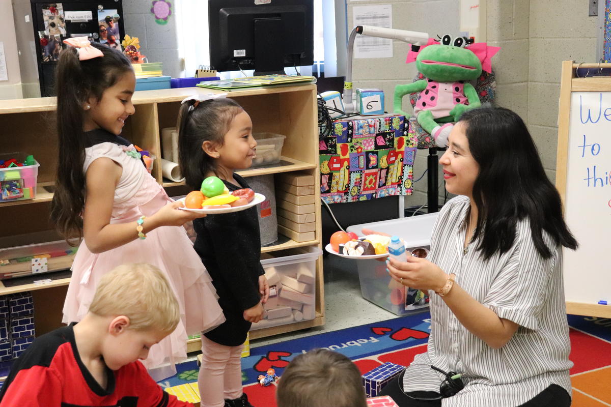 Prk-K teacher serving play food to students.