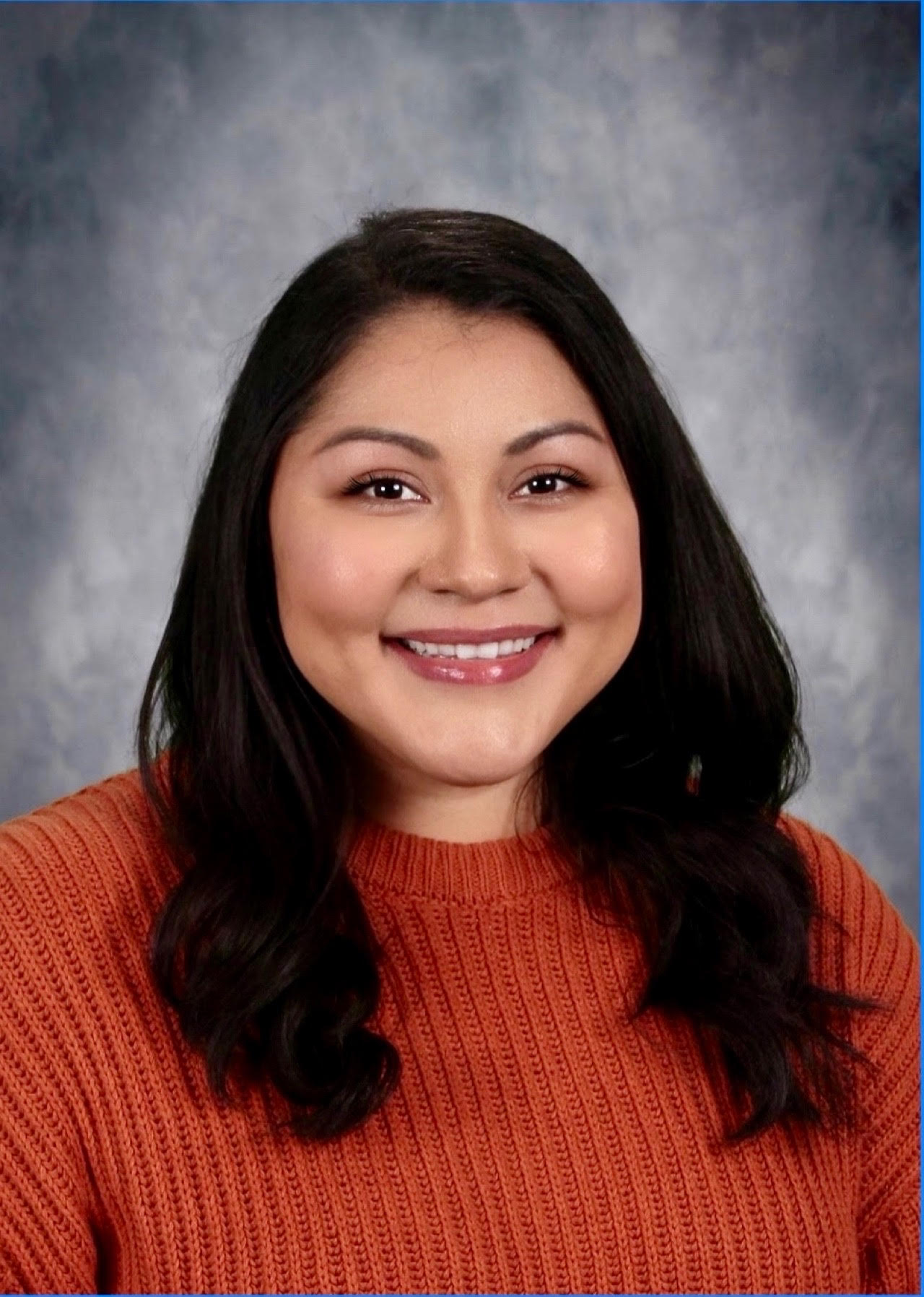 A hispanic woman with long black har wearing a red sweater.